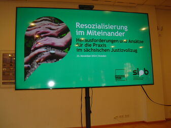 Auf einem Monitor steht auf grünem Hintergrund: Resozialisierung im Miteinander – Herausforderungen und Ansätze für die Praxis im sächsischen Justizvollzug