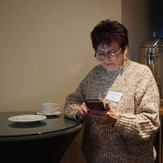 Ein Frau steht an einem Tisch und schaut auf ihr Handy